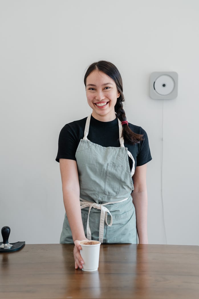 Happy ethnic female barista offering coffee in paper cup